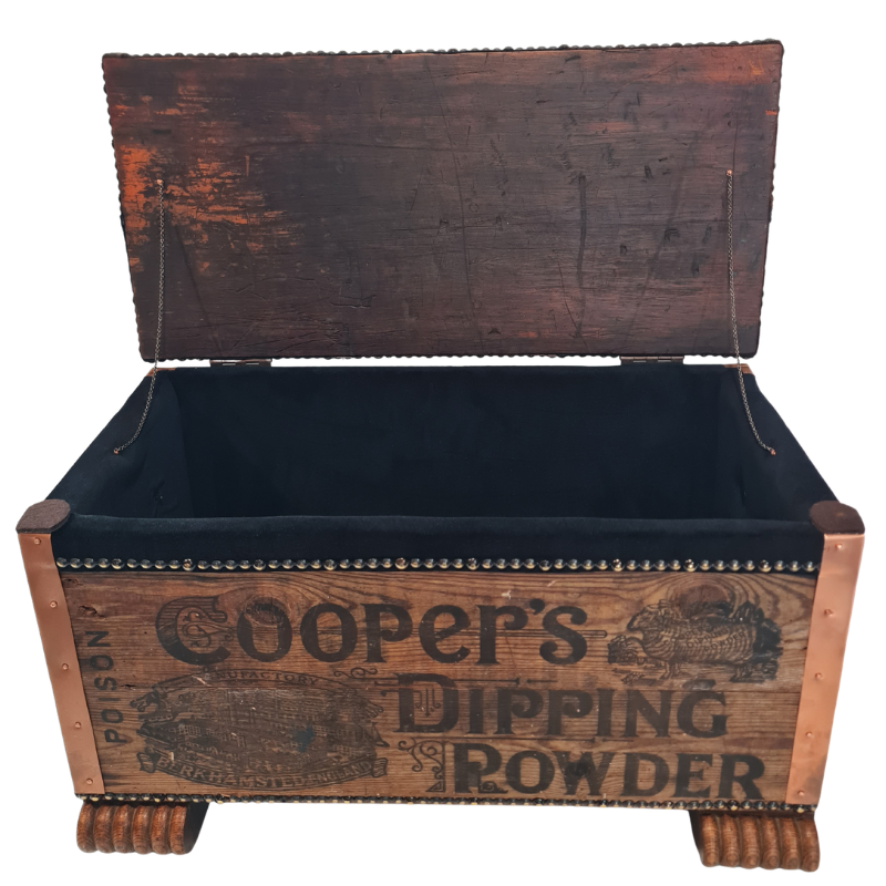 A rustic wooden storage chest with an open lid, featuring a dark black velvet interior and the vintage text 'Cooper's Dipping Powder' printed on the front, set against a plain background.