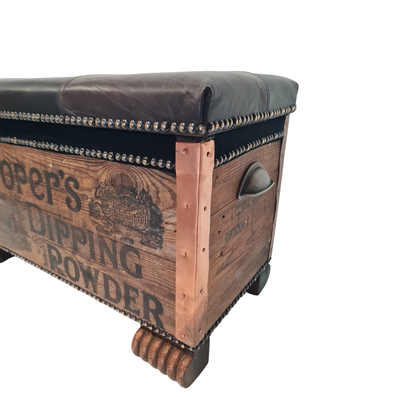 A rustic wooden storage chest with a dark brown leather bench top, copper-colored metal corner brackets, nailhead trim, and vintage-style printed text reading 'Operator's Dipping Powder' on a white background.