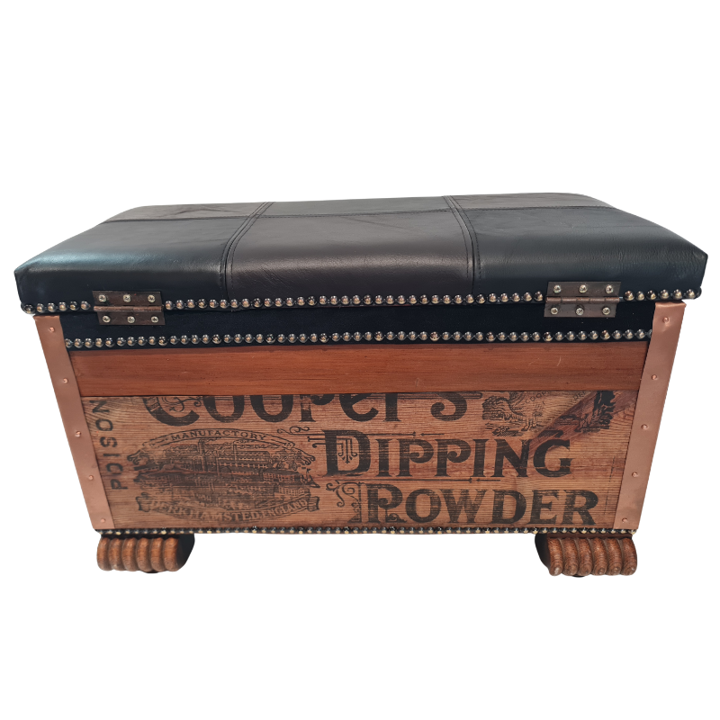 A rustic wooden storage chest or bench with a black leather top, brass nailhead trim, and vintage-style printed text on the front panel.