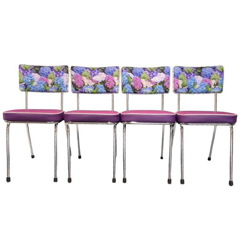 Four matching mid-century modern dining chairs with purple vinyl seats and  hydrangea floral backrests featuring blue, pink, and purple hydrangeas on a white background.