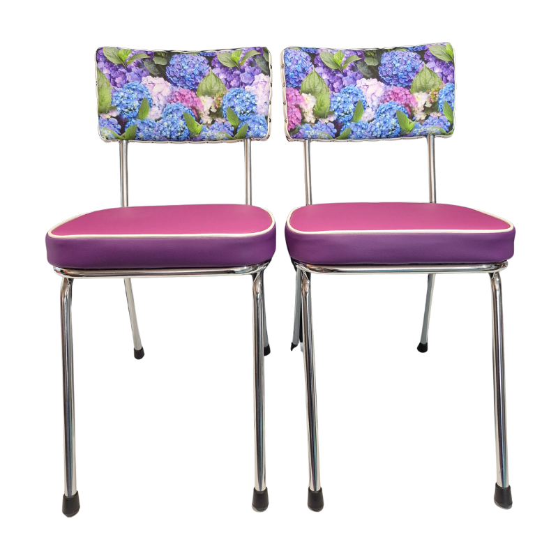 Two matching kitchen chairs with purple-pink upholstered seats and hydrangea floral backrests, supported by chrome metal legs, shown against a plain white background.