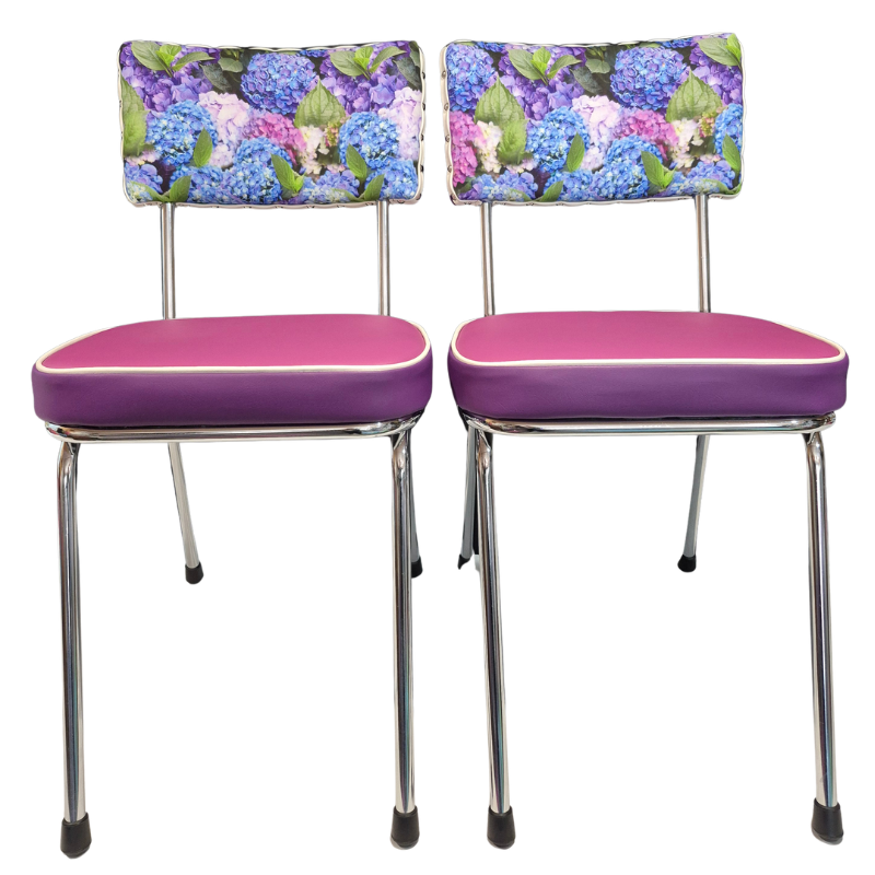 Two matching mid-century modern dining chairs with purple vinyl seats, chrome legs, and hydrangea floral patterned fabric backrests featuring blue, purple, and pink hydrangeas.