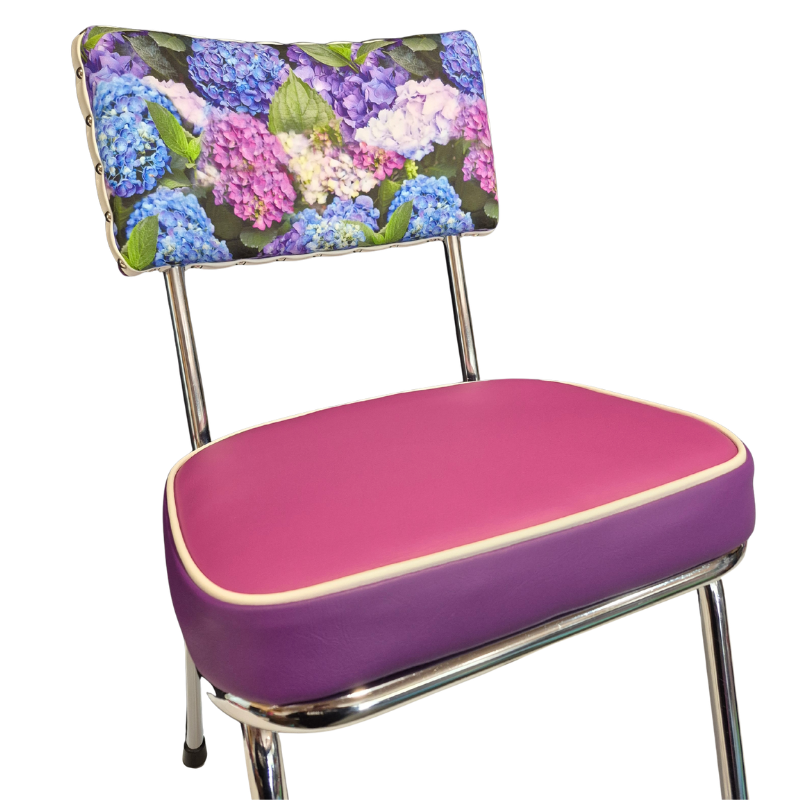 A retro-style metal chair with a bright pink and purple upholstered seat, a hydrangea floral-patterned backrest cushion featuring blue, purple, and pink hydrangeas, and shiny chrome legs.
